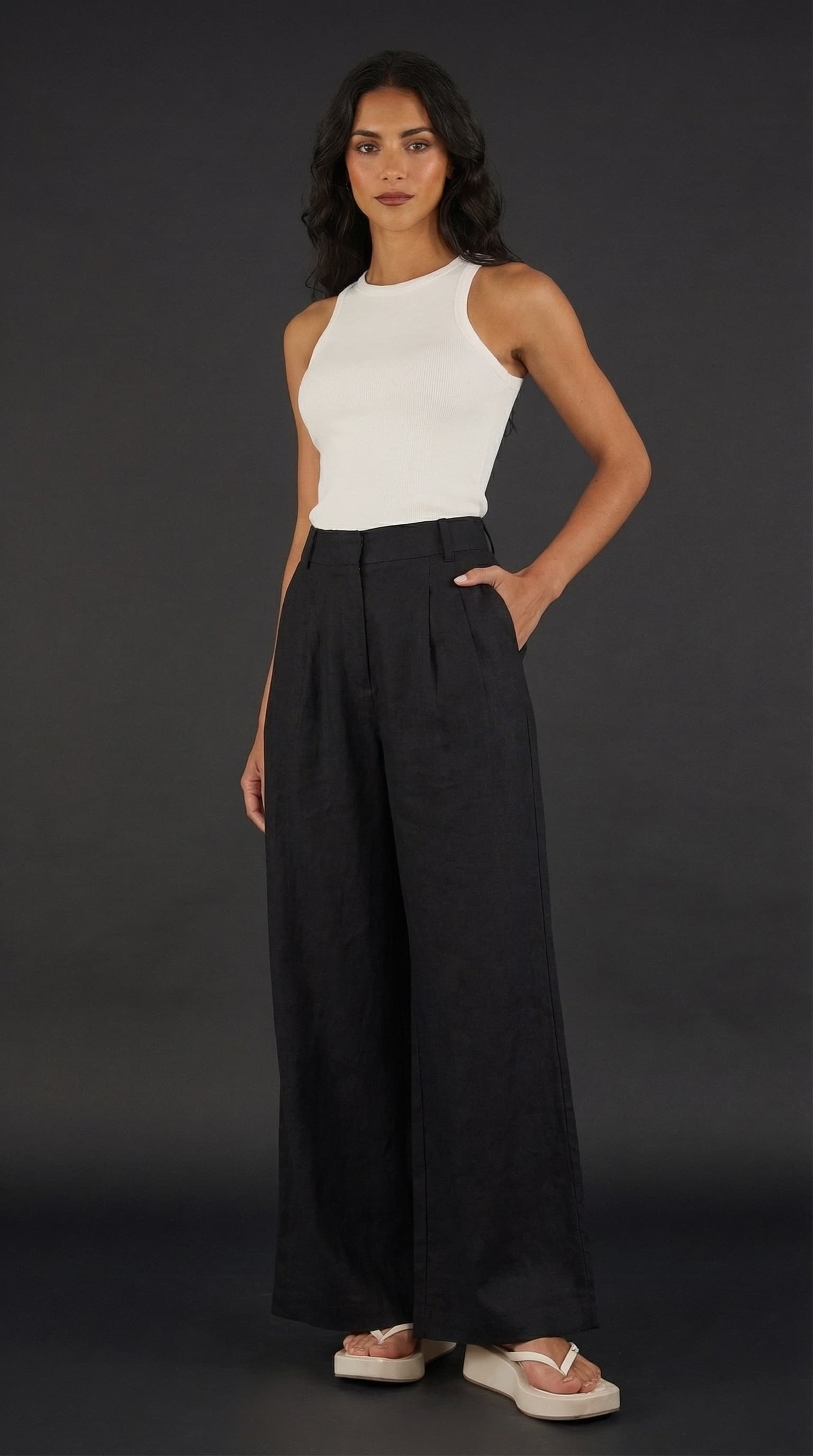 Studio portrait of a model in a white tank and black wide-leg linen trousers